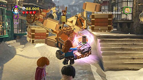 Ze środka torby wyciągamy maszynę do mielenia drewna, pozostaję ją nakręcić, korbę znajdziemy tuż obok maszyny - Powrót do szkoły | Opis przejścia - Rok 7 | LEGO Harry Potter Lata 5-7 - LEGO Harry Potter: Lata 5-7 - poradnik do gry