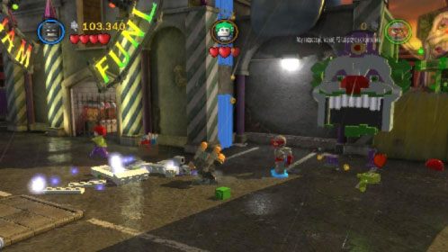 Po oddaniu strzału skieruj się w prawy górny narożnik placu i ułóż z klocków na ziemi podobiznę Jokera na ścianie (obrazek) - Współudział | Opis przejścia LEGO Batman 2 DC Super Heroes - LEGO Batman 2: DC Super Heroes - poradnik do gry