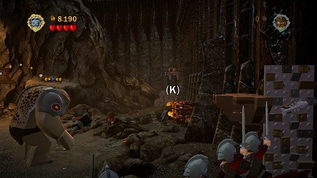 Gdy walka przeniesie się na lewo, wystarczy pociągnąć Szagratem za znajdującą się w tej części lokacji pomarańczową rękojeść a skrzynia będzie nasza - Czarna Brama | Znajdźki | LEGO The Lord of the Rings - LEGO The Lord of the Rings: Władca Pierścieni - poradnik do gry